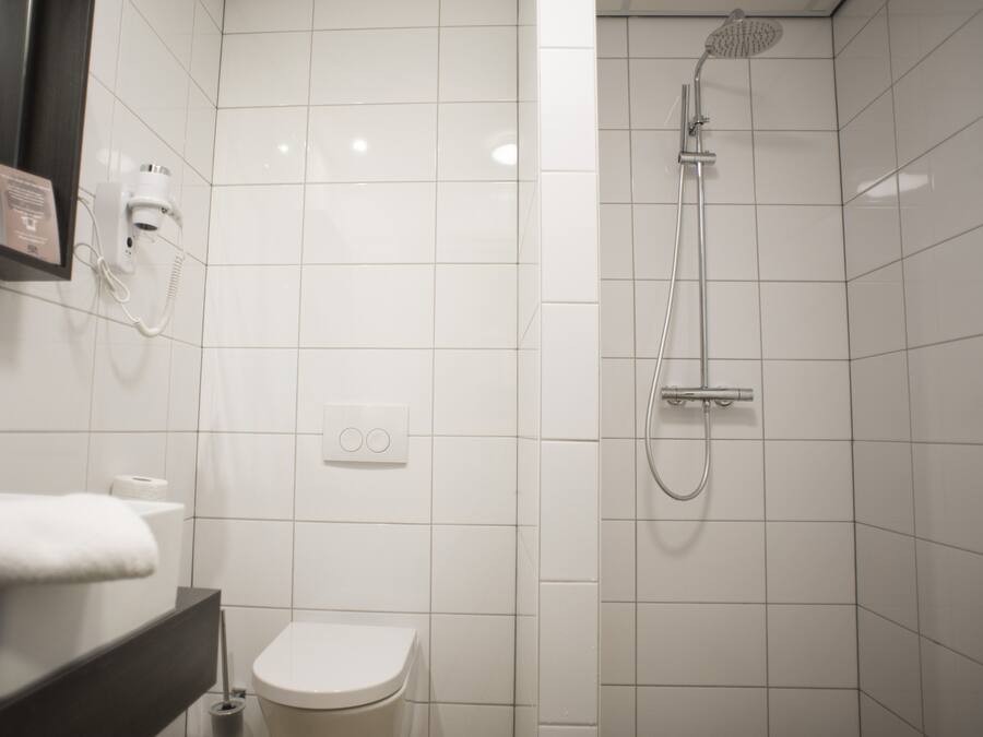 A modern bathroom with a toilet, a sink, a mirror, a hairdryer, and a shower.