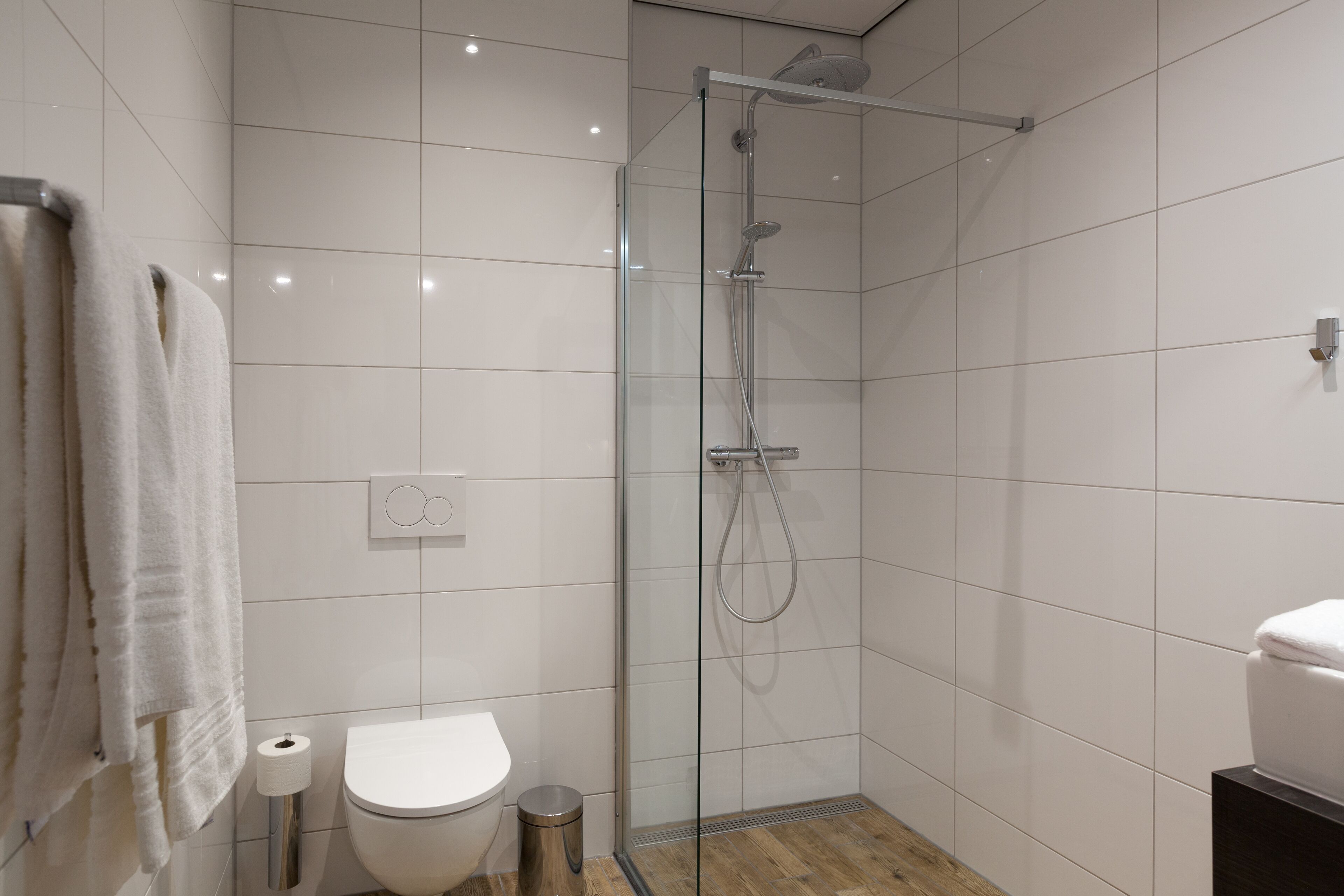 A modern bathroom with a glass-enclosed shower, a toilet, and a towel rack.