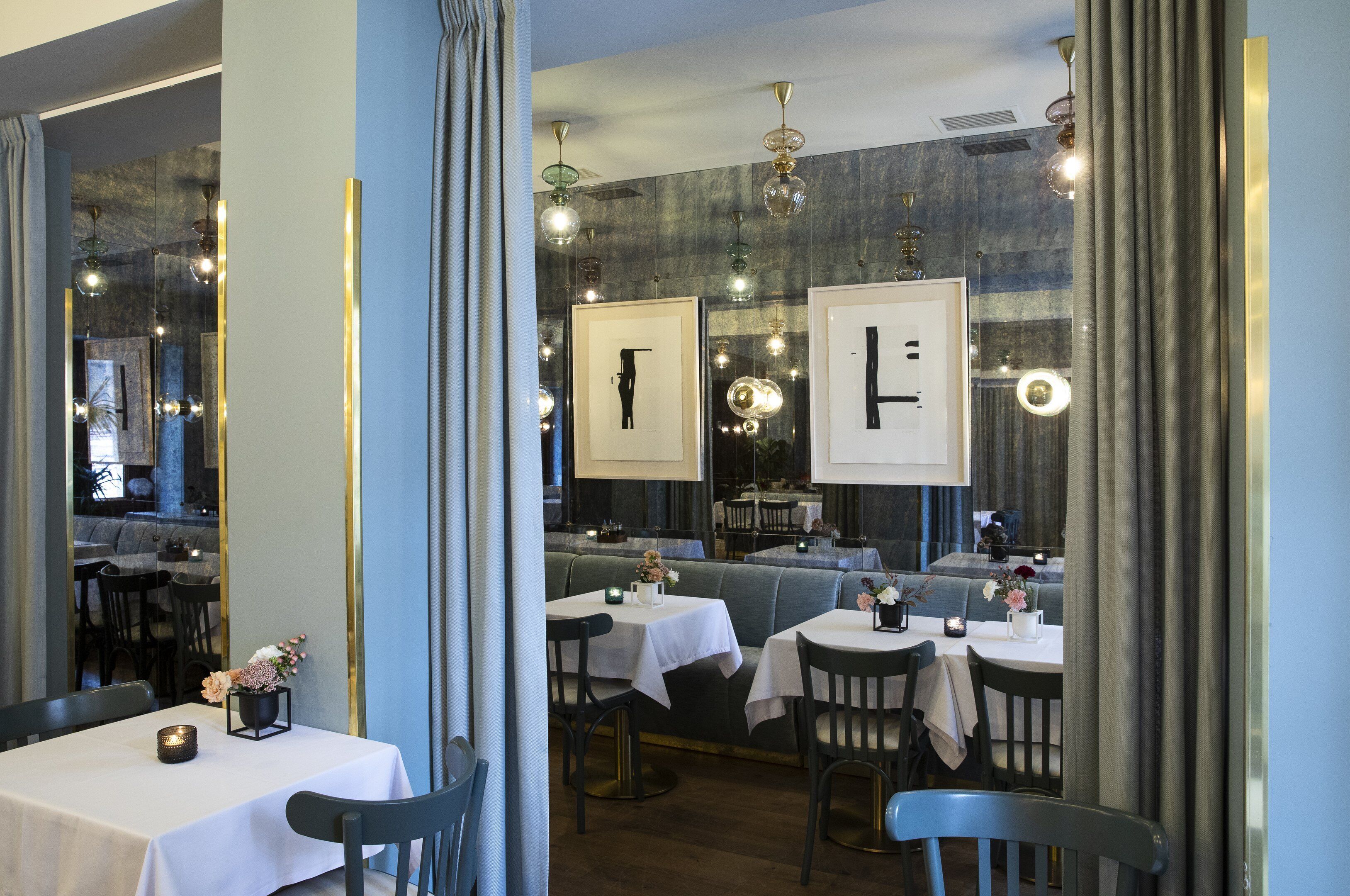 A restaurant with tables and chairs, framed artwork on the walls, and hanging light fixtures.