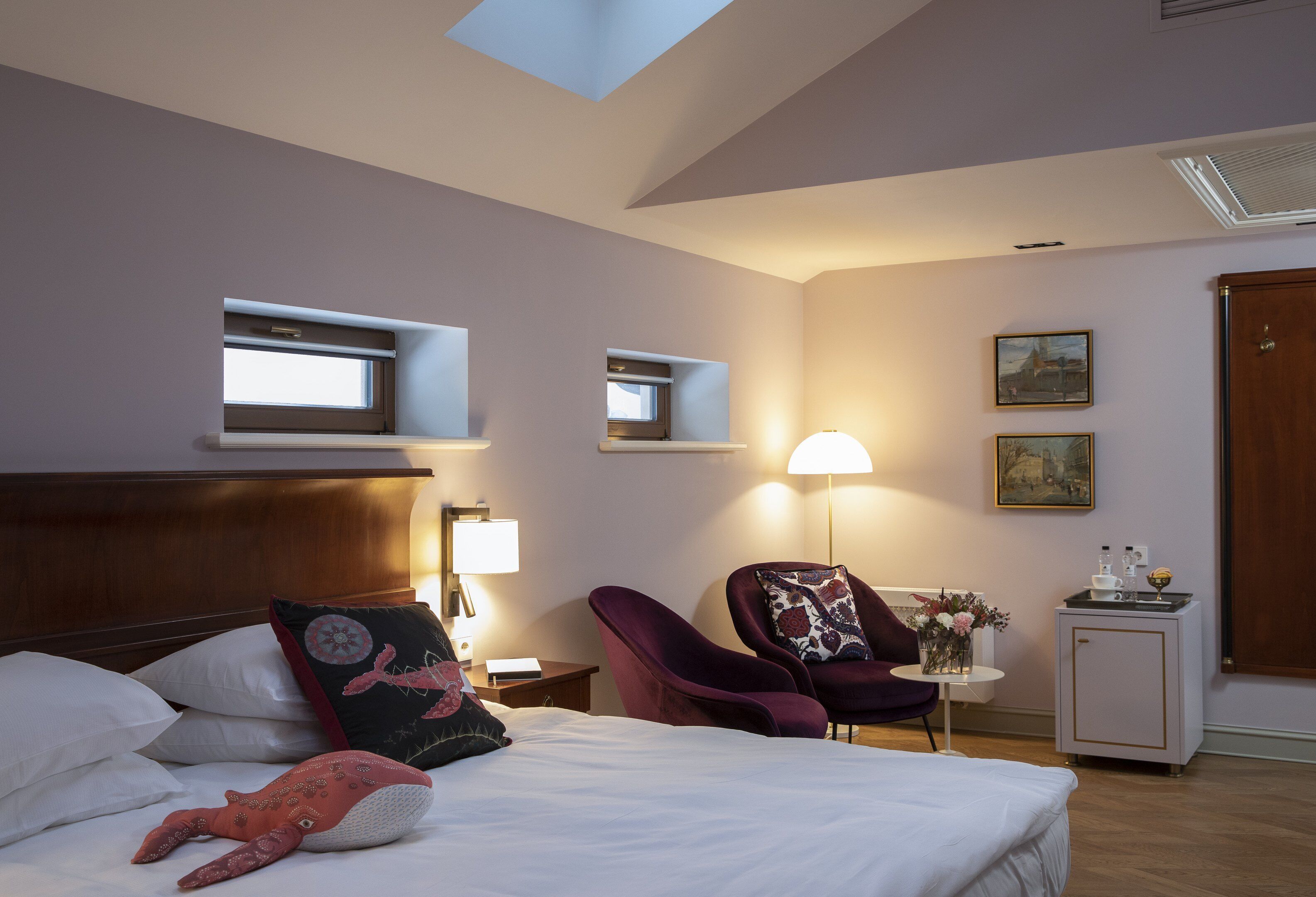 Una habitación de hotel con una cama, dos sillas, una mesita, una lámpara y un armario.