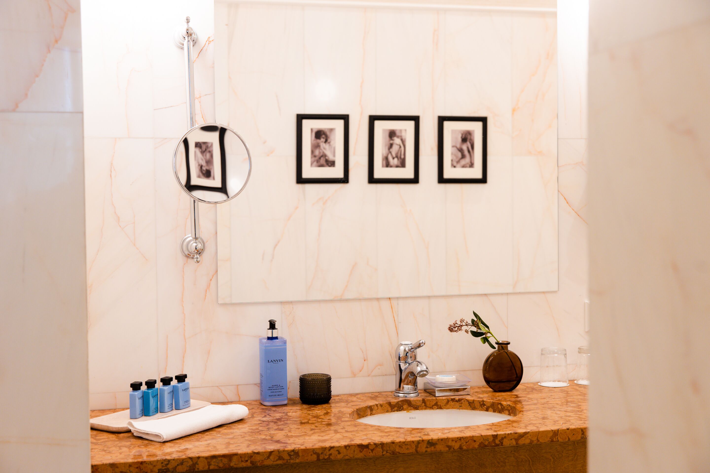 A bathroom with a marble wall, a sink with a faucet, a mirror, and three framed pictures on the wall.