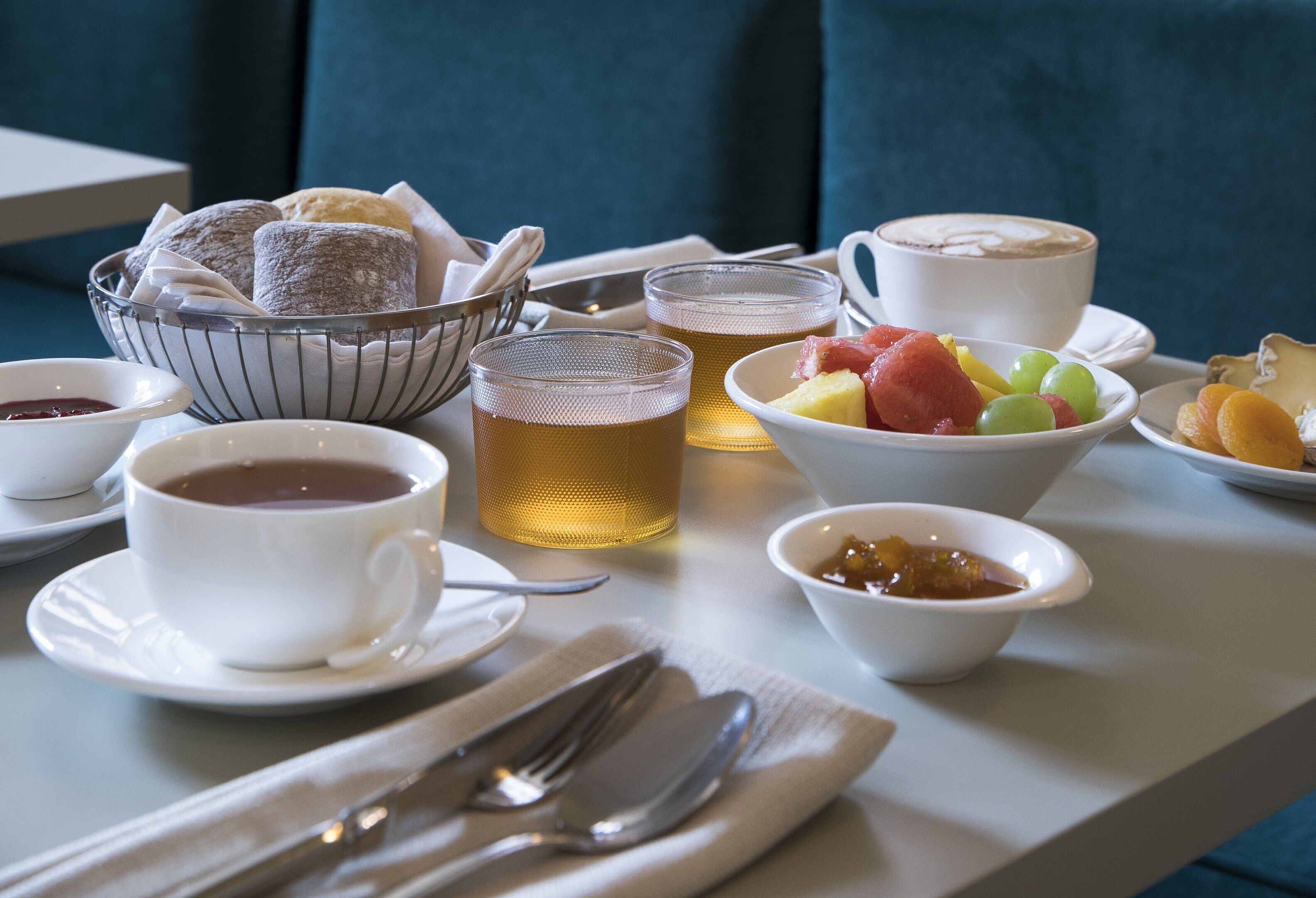A breakfast setting with a bowl of pastries, cups of coffee and tea, and a fruit bowl.