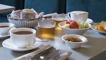 A breakfast setting with a bowl of pastries, cups of coffee and tea, and a fruit bowl.