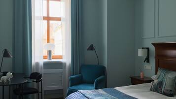 A hotel room with a bed, a desk, a chair, a lamp, and a nightstand.
