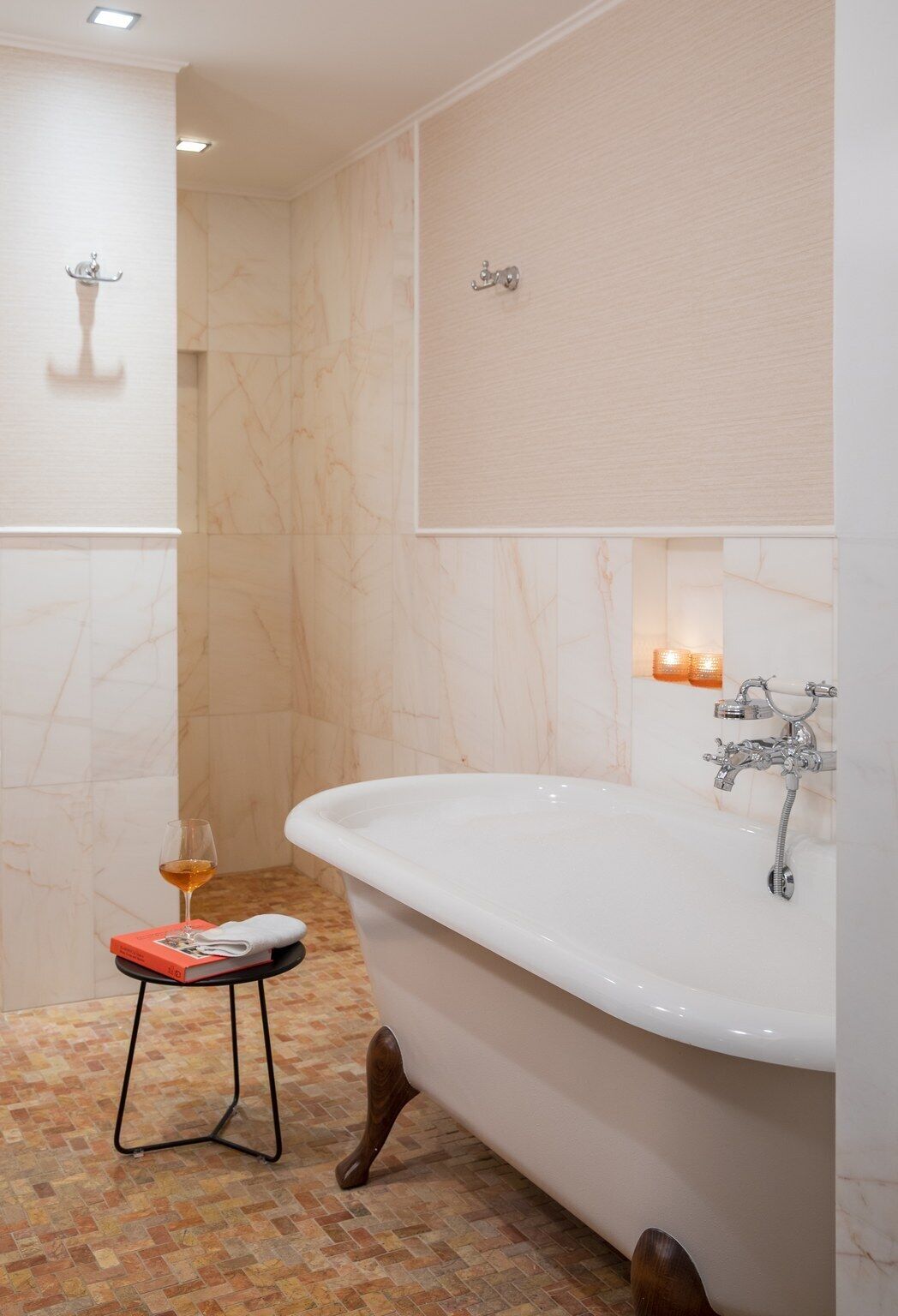A modern bathroom with a freestanding bathtub, a small stool with a book and glass, and a towel on the floor.