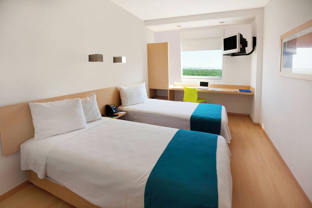 Habitación de hotel con dos camas, un escritorio, una silla, un televisor y una ventana con vistas.