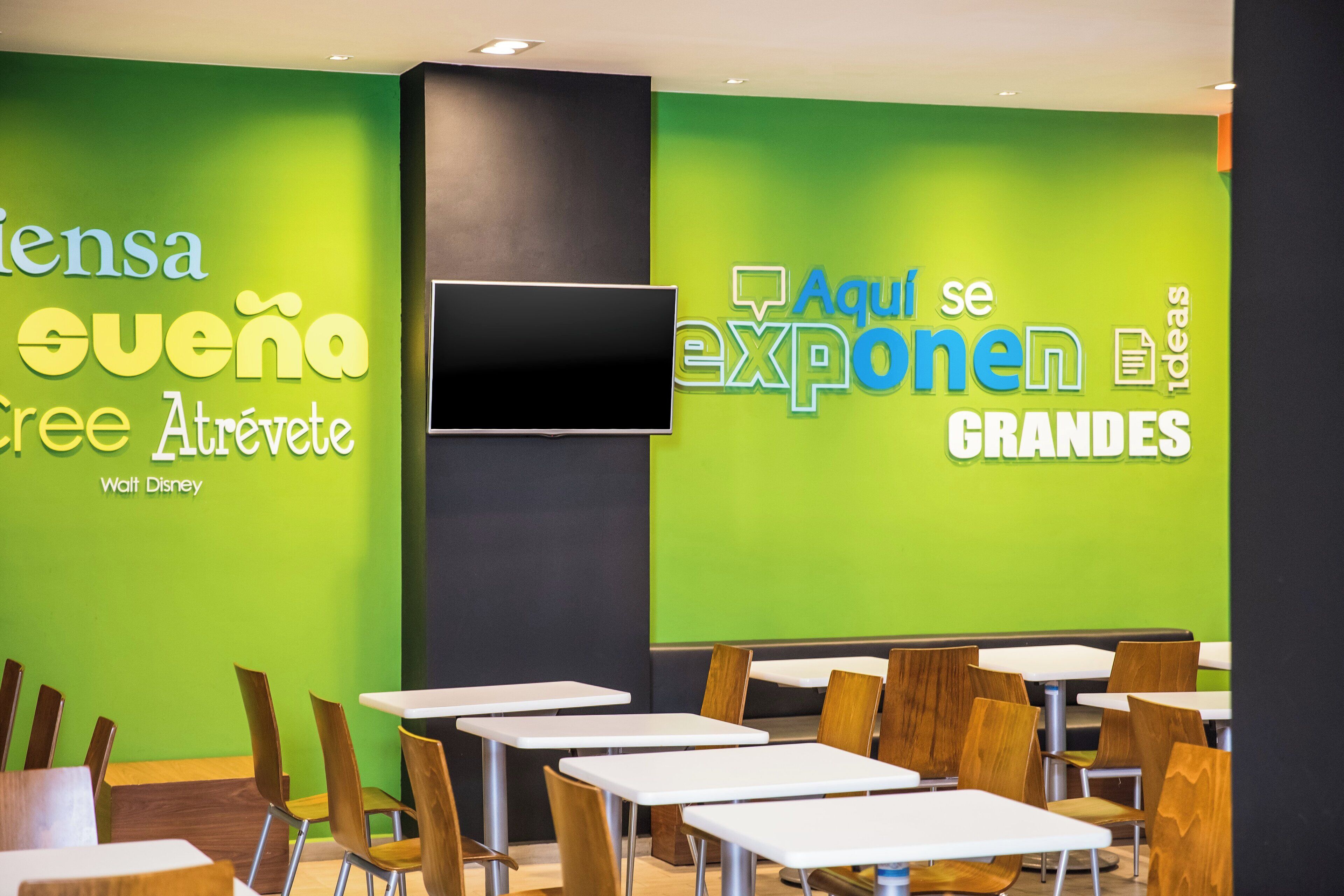 A modern dining area with green walls, white tables, and wooden chairs.