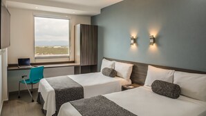 A hotel room with two beds, a desk with a laptop, a chair, and a large window offering a city view. - One Monterrey Aeropuerto (Apodaca)