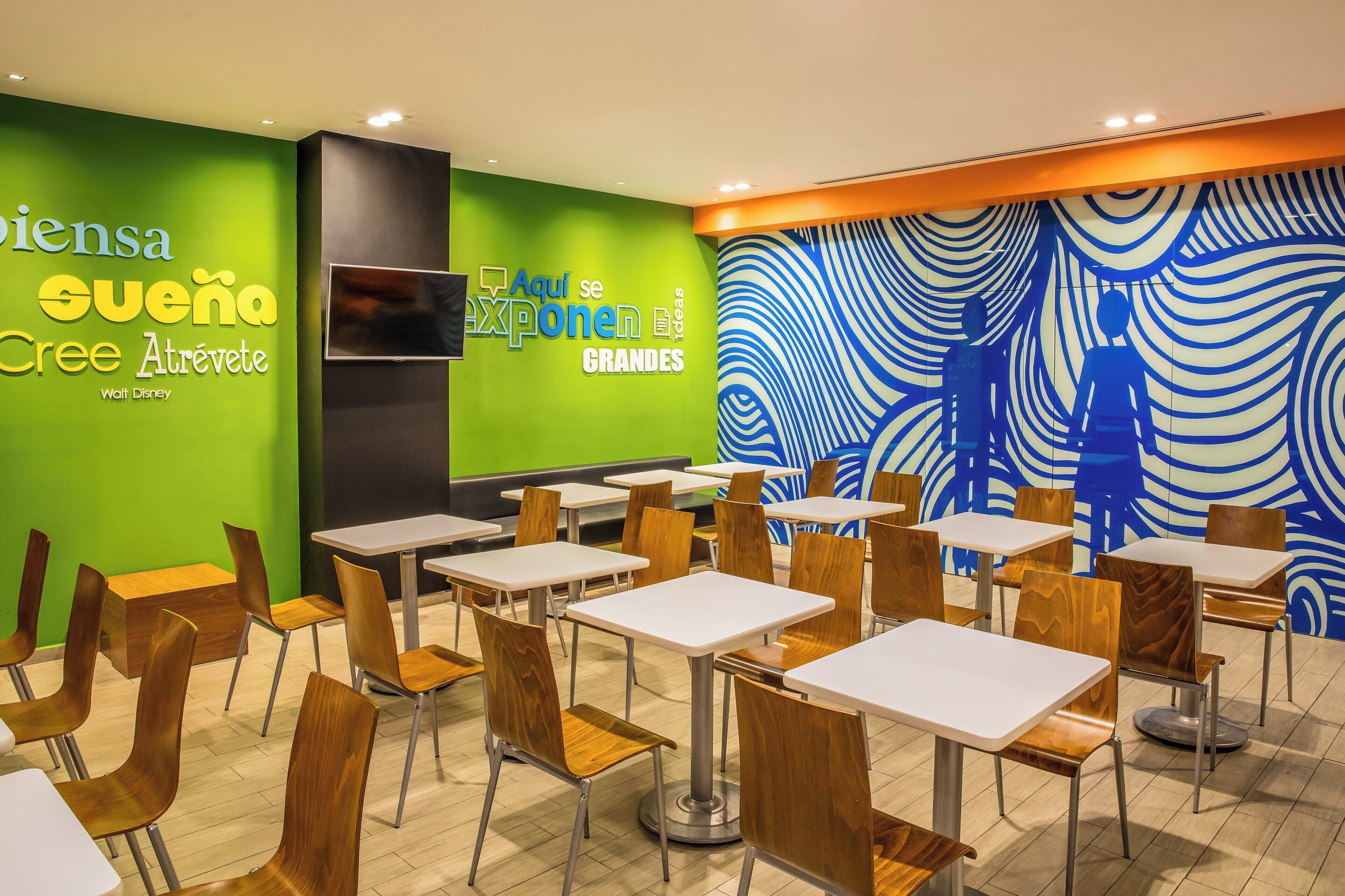 A modern dining area with green and blue wall art, wooden chairs, and white tables.