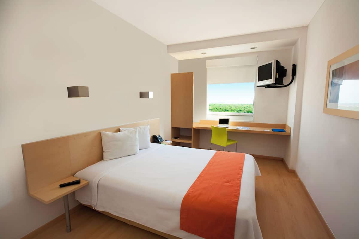 Una habitación de hotel con cama, escritorio, silla, televisión y ventana con vistas.