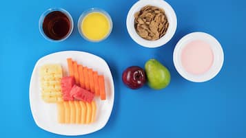 Une assiette contenant des fruits et des légumes coupés en tranches, deux pommes et deux verres de jus, le tout sur un fond bleu.