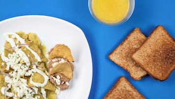 A plate of nachos with cheese and red onions, accompanied by slices of toast and a glass of orange juice on a blue background.