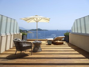 Una terraza de madera con vista al mar, una silla de mimbre, un sillón de descanso y una sombrilla.