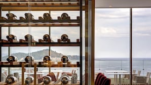 Una bodega con botellas, una mesa con sillas y vista al mar.