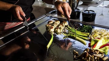 Ein Koch bereitet Essen auf einem offenen Grill mit Gemüse und Knödeln zu.
