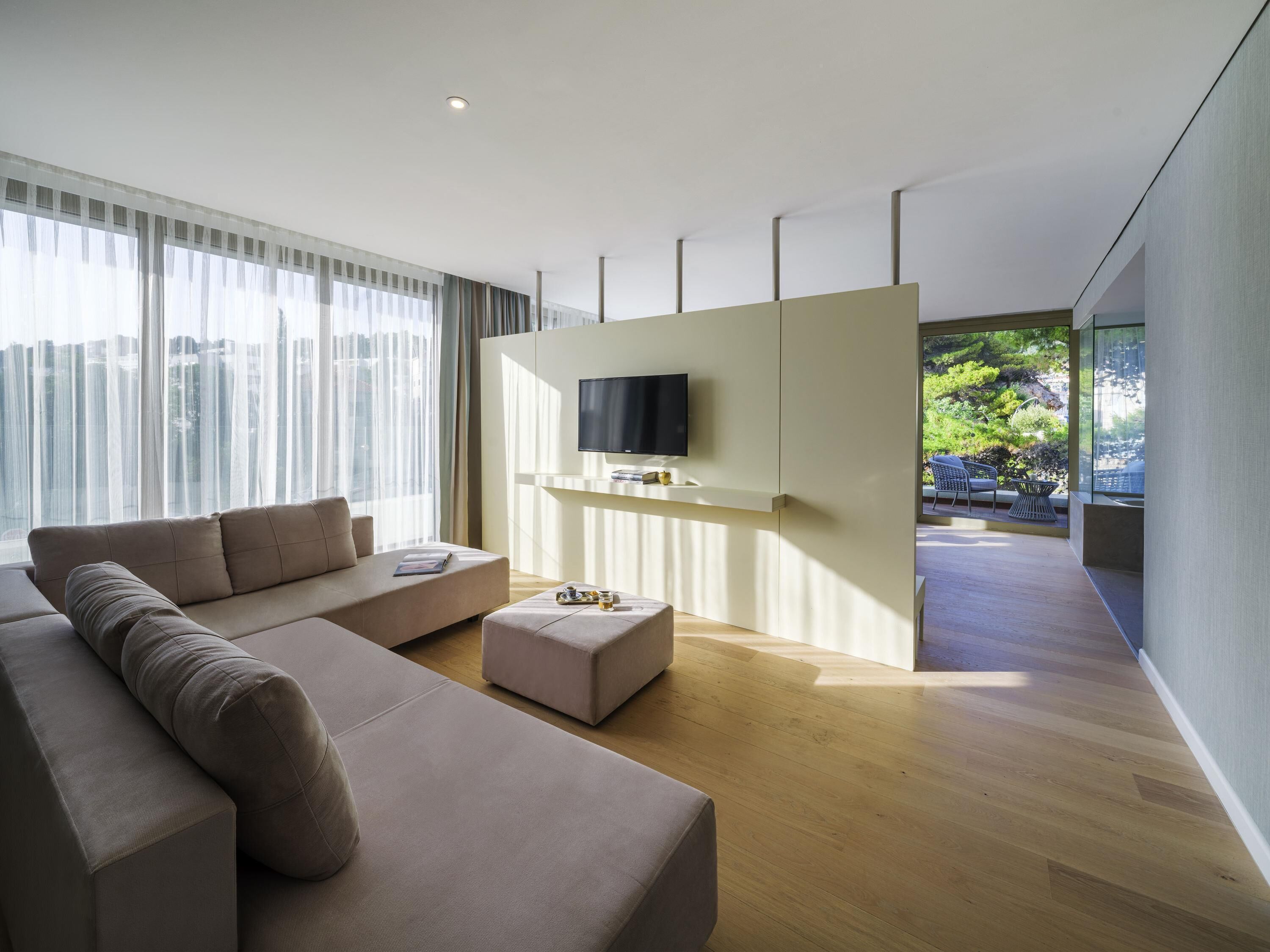 A modern living room with a sofa, ottoman, and a flat-screen TV mounted on a wall.