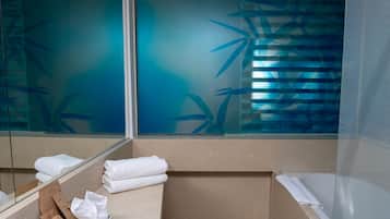 A modern bathroom with a large mirror, a bathtub, and a toilet. There are towels and toiletries on the counter.