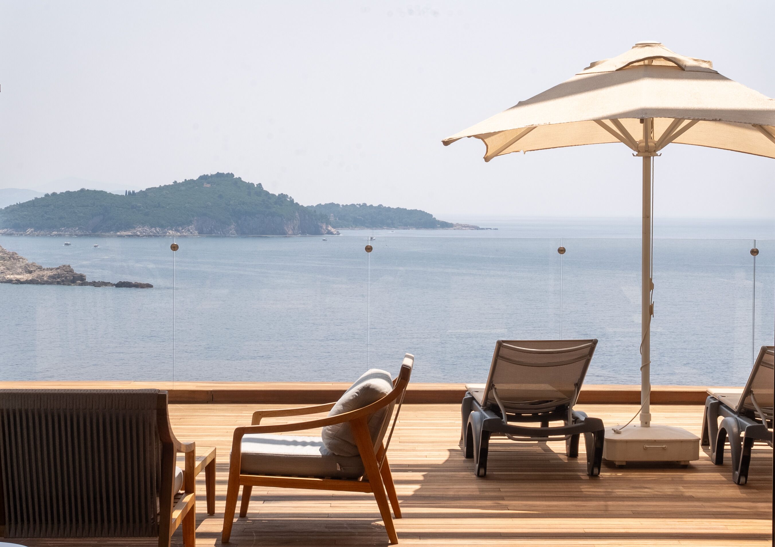 A deck with wooden flooring, two lounge chairs, and a large umbrella providing shade.
