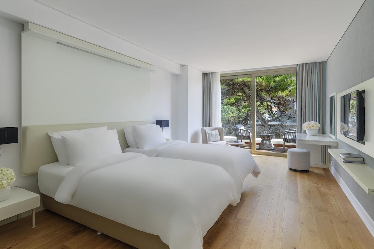 Une chambre d’hôtel moderne dotée d’un grand lit, d’une télévision, d’un bureau et d’un balcon offrant une vue sur les arbres.