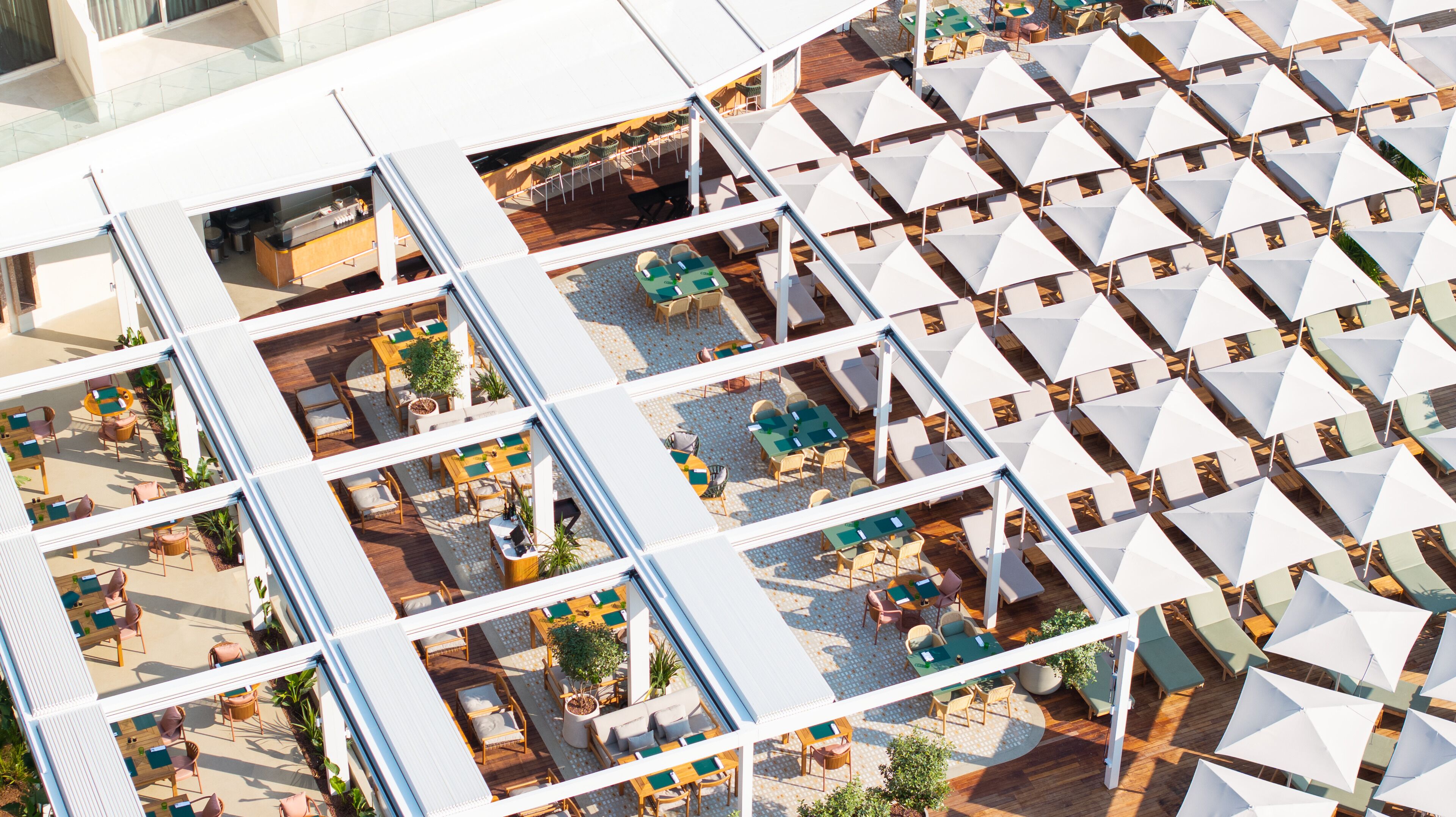 Une terrasse sur le toit dotée de plusieurs espaces aménagés, comprenant des tables et des chaises, ainsi qu’un coin agrémenté de parasols blancs.
