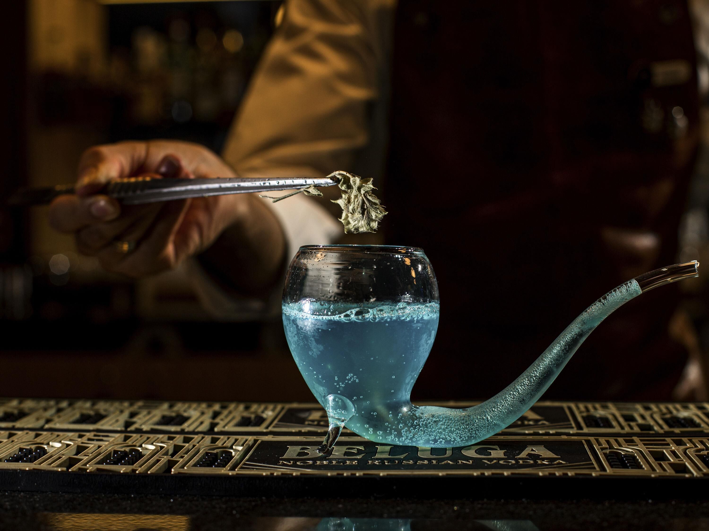 A bartender pouring a blue liquid into a glass with a long stem, with a bar mat labeled 'BELUGA' beneath.