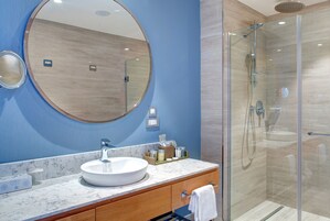 Un baño moderno con un espejo redondo, un lavamanos blanco y una ducha con mampara de vidrio.