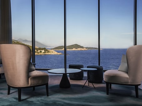 A room with two armchairs, a small round table, and a view of the sea and distant hills.