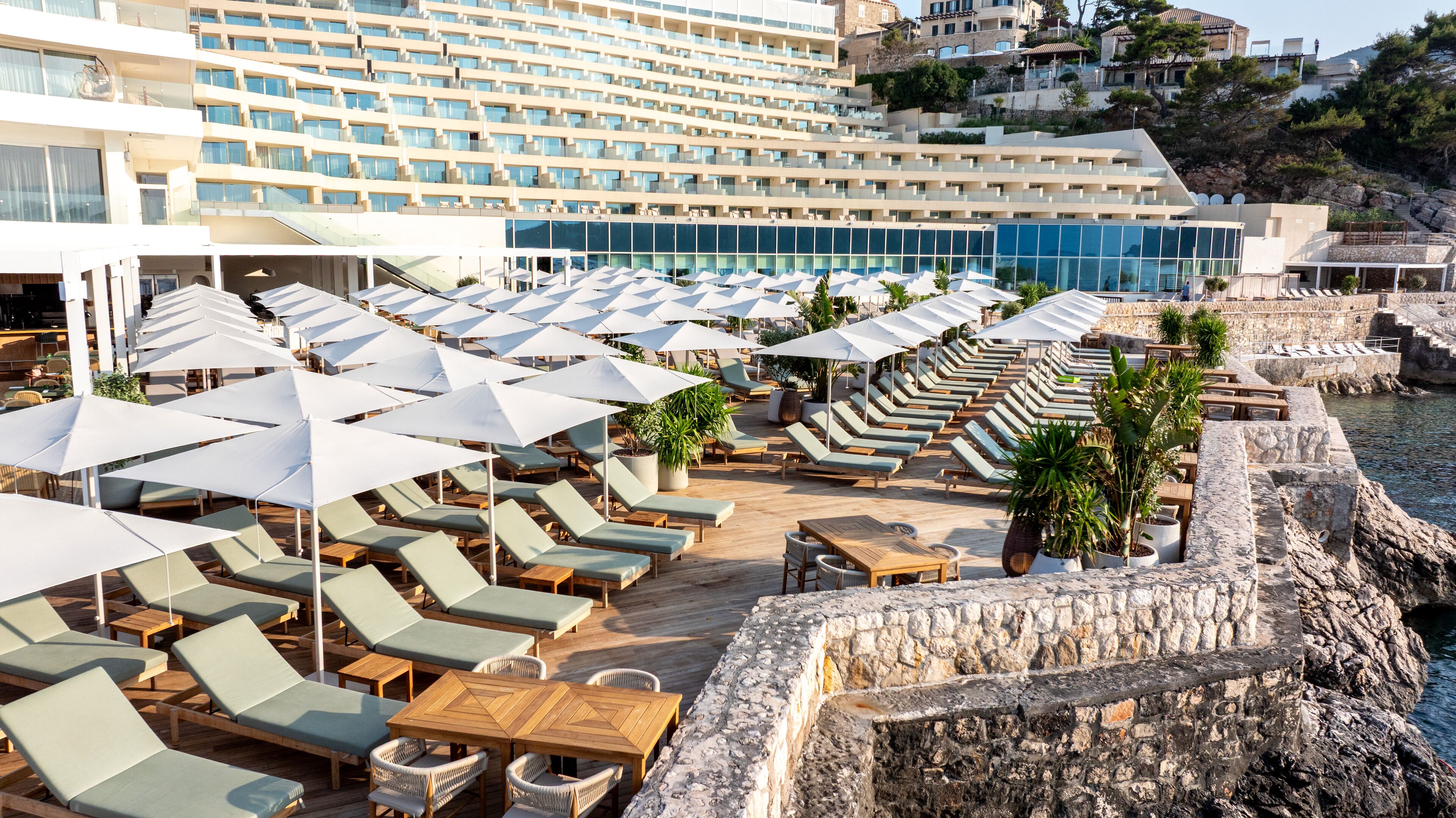 A resort with rows of sun loungers and umbrellas, a pool area, and a view of the sea.