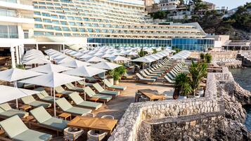 A resort with rows of sun loungers and umbrellas, a pool area, and a view of the sea.