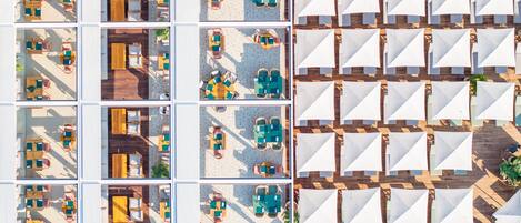 Vista aérea de un hotel con varias zonas de comedor, mesas al aire libre y diferentes distribuciones de mesas y sillas.