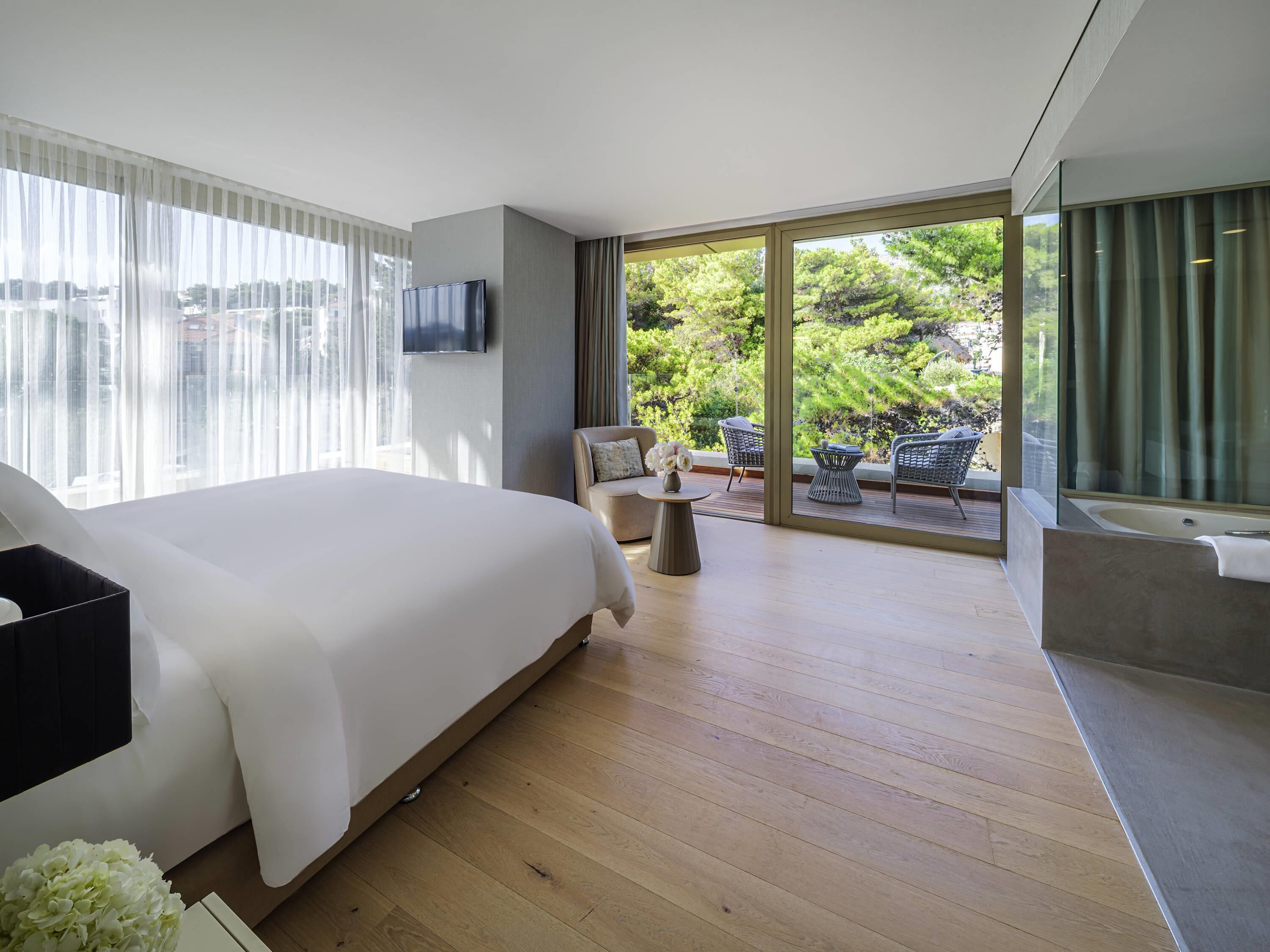 A modern bedroom with a large bed, a TV, and a balcony with outdoor seating.