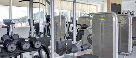 Un gimnasio con diversos equipos de ejercicio, incluyendo mancuernas, una prensa de banca y una máquina de poleas.