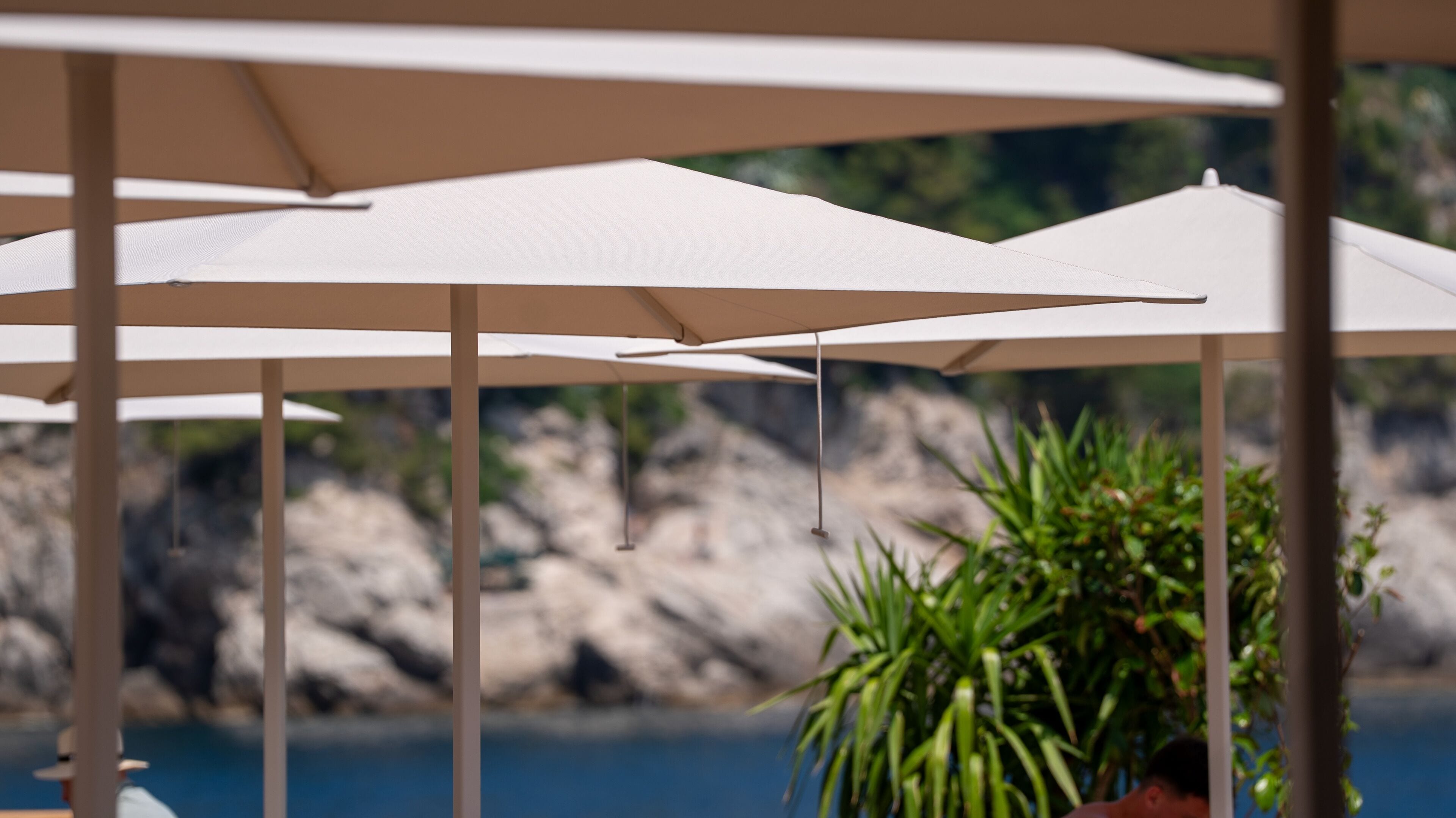 A series of white umbrellas with a rocky landscape and a body of water in the background.
