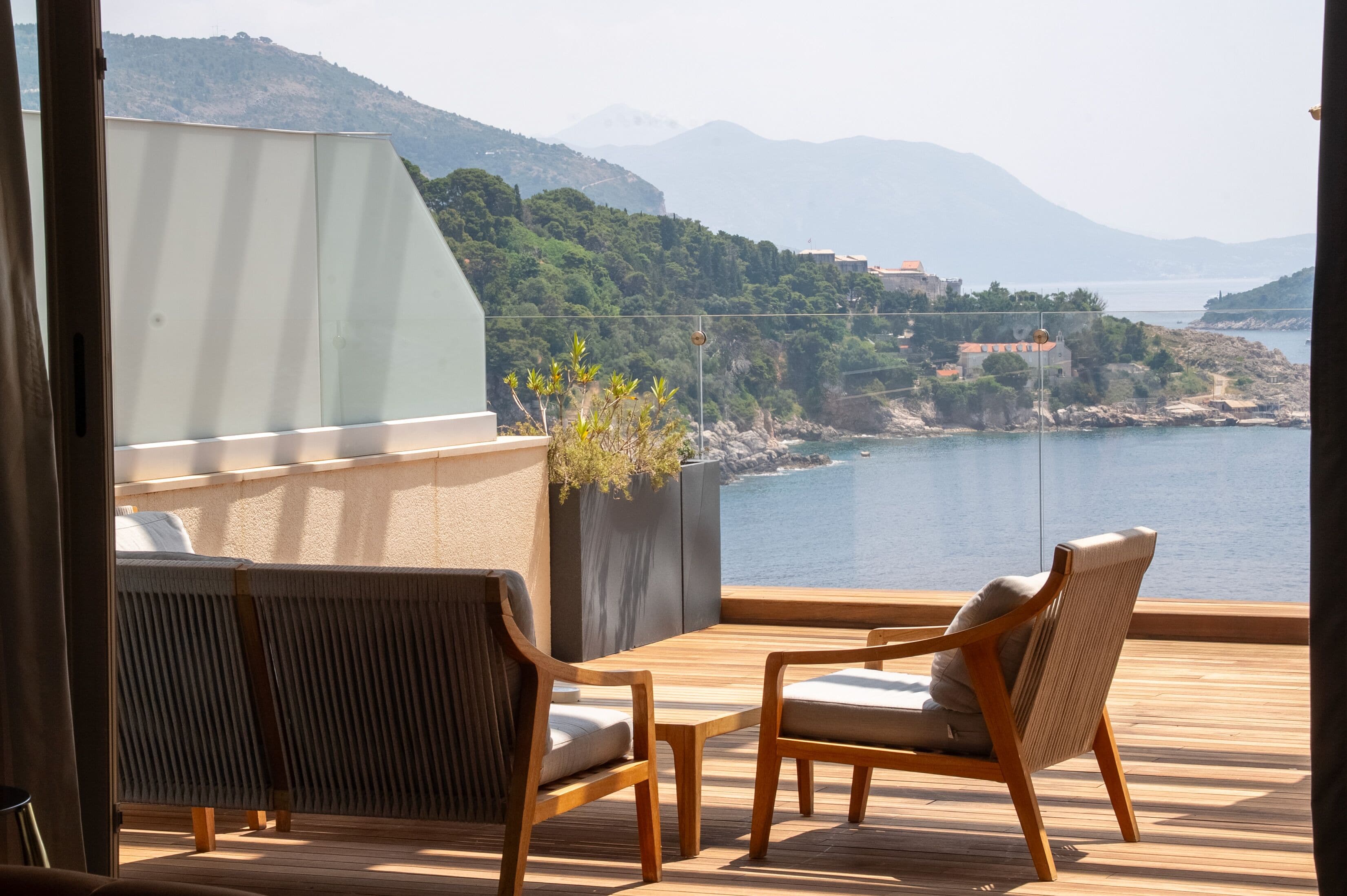A balcony with wooden furniture and a view of a coastal landscape.