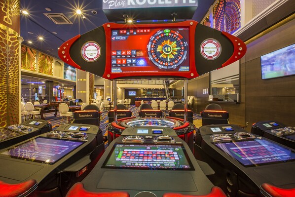A casino with multiple gaming tables and a large roulette wheel.