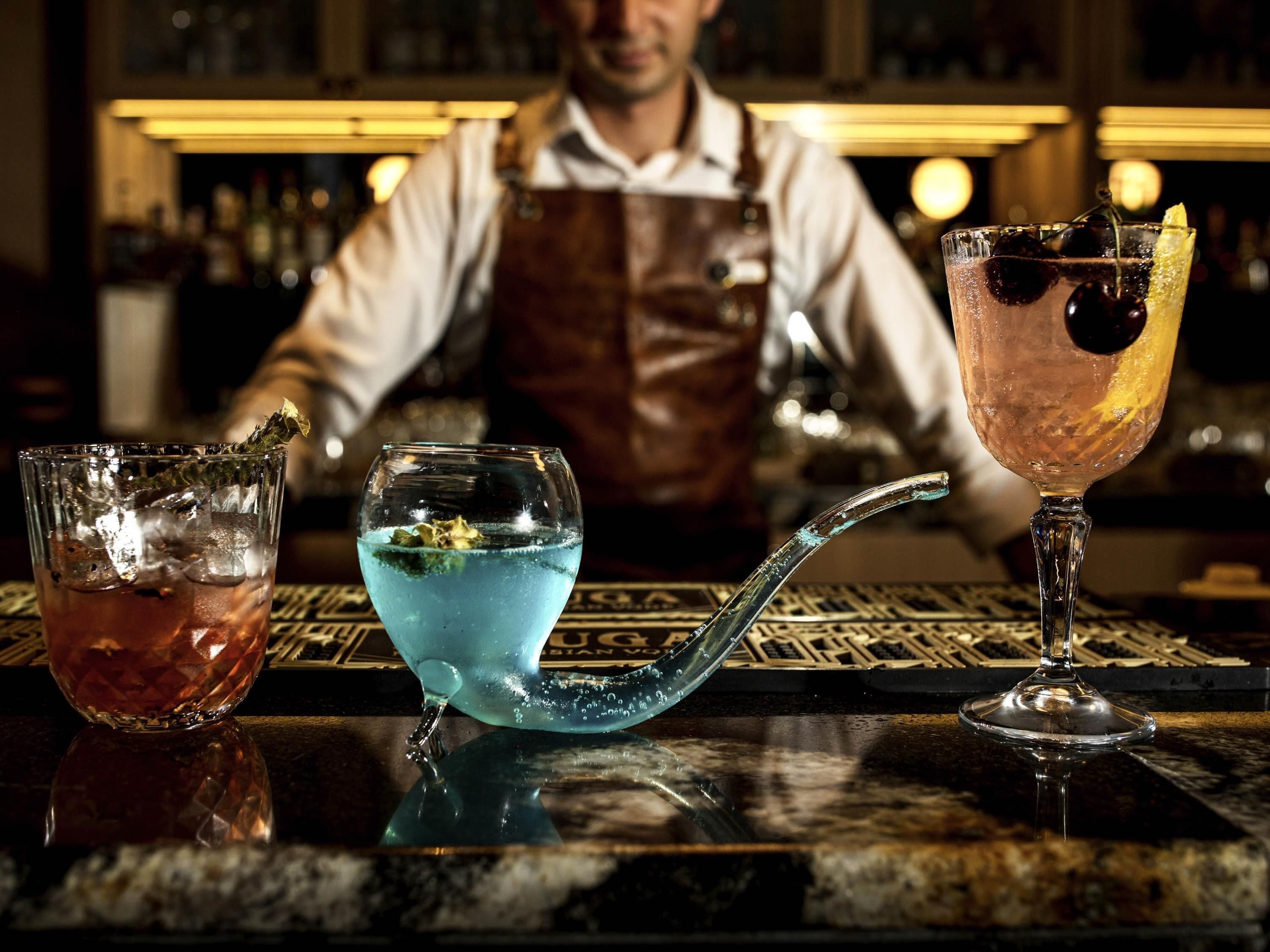 Three drinks on a bar counter with a bartender in the background.