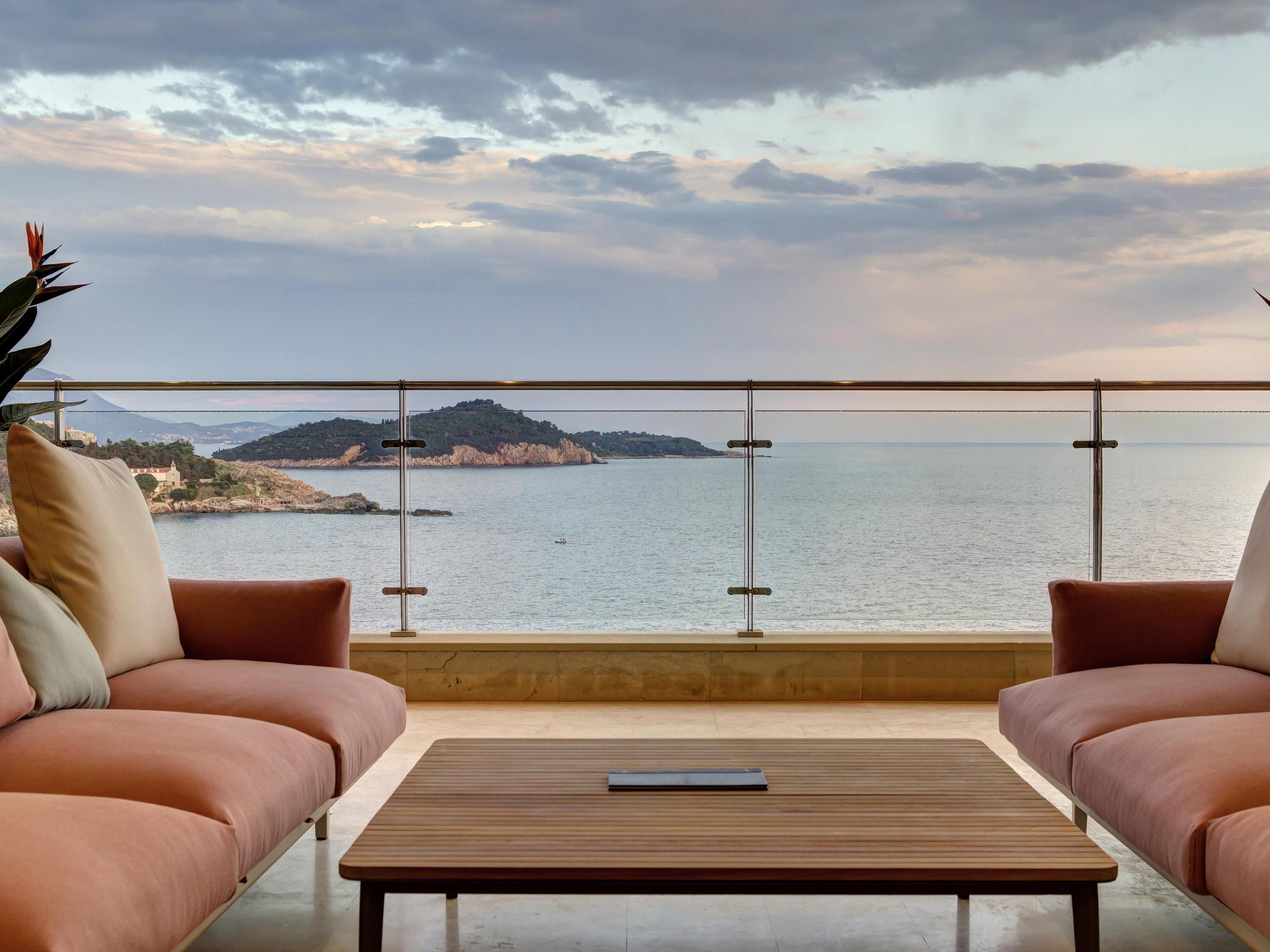 Un balcon avec vue sur la mer et une île au loin, aménagé avec deux canapés et une table basse.