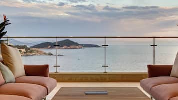 Un balcon avec vue sur la mer et une île au loin, aménagé avec deux canapés et une table basse.