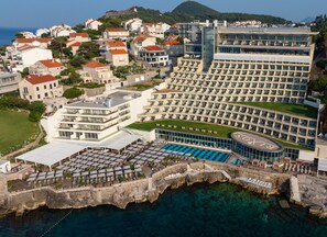 Un hotel frente al mar con una piscina grande, varios balcones y vistas al océano.