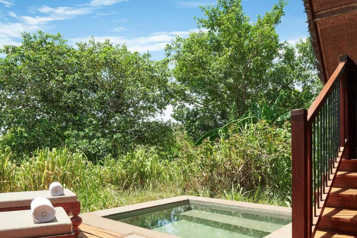 A wooden deck with a hot tub, lounge chairs, and a staircase.