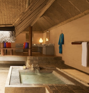 Un espacio de spa con una bañera de hidromasaje de piedra, techo de madera y estructura de techo de paja.