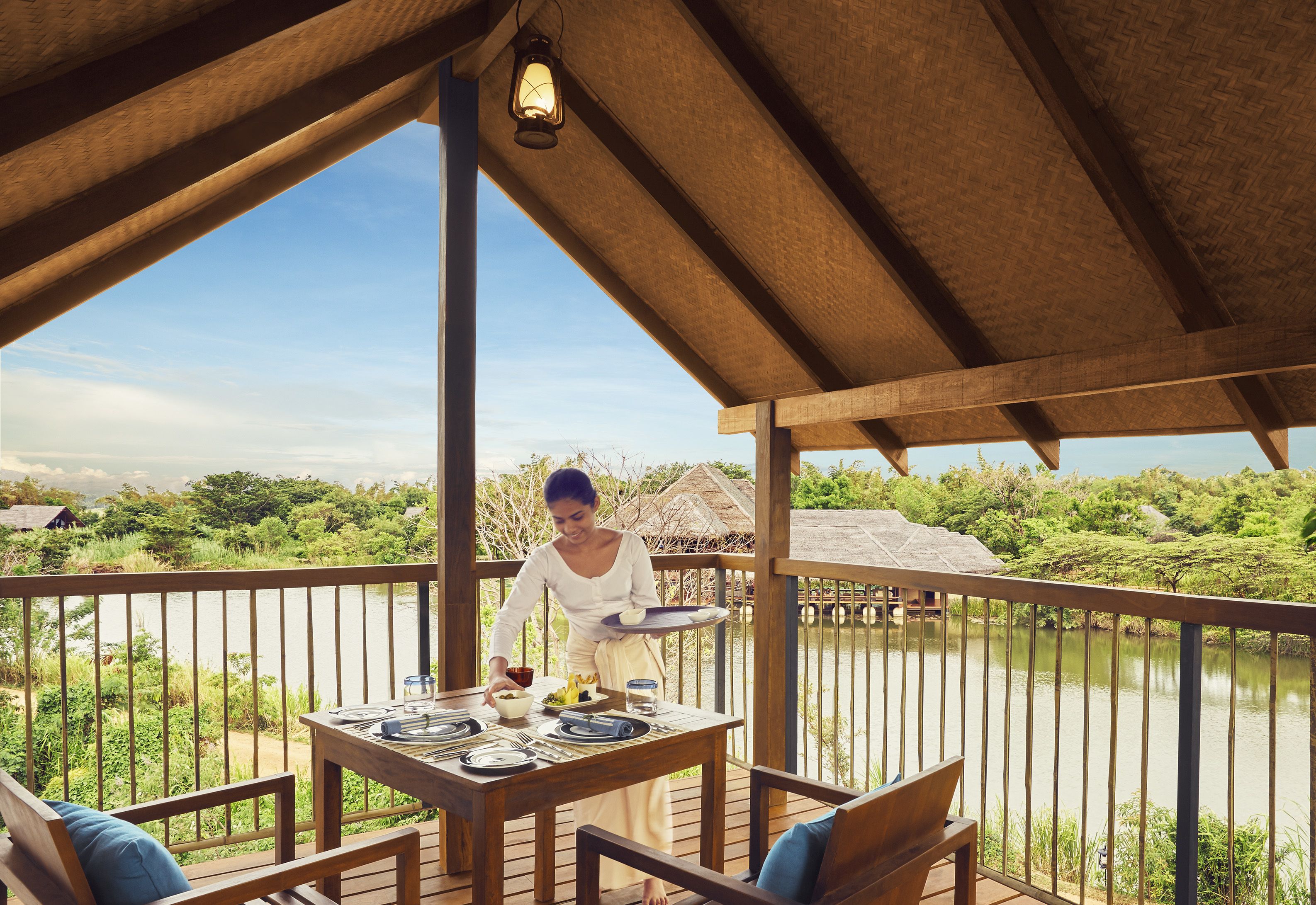 Une terrasse en bois avec une table dressée pour le repas, offrant une vue sur une étendue d’eau et une végétation luxuriante.