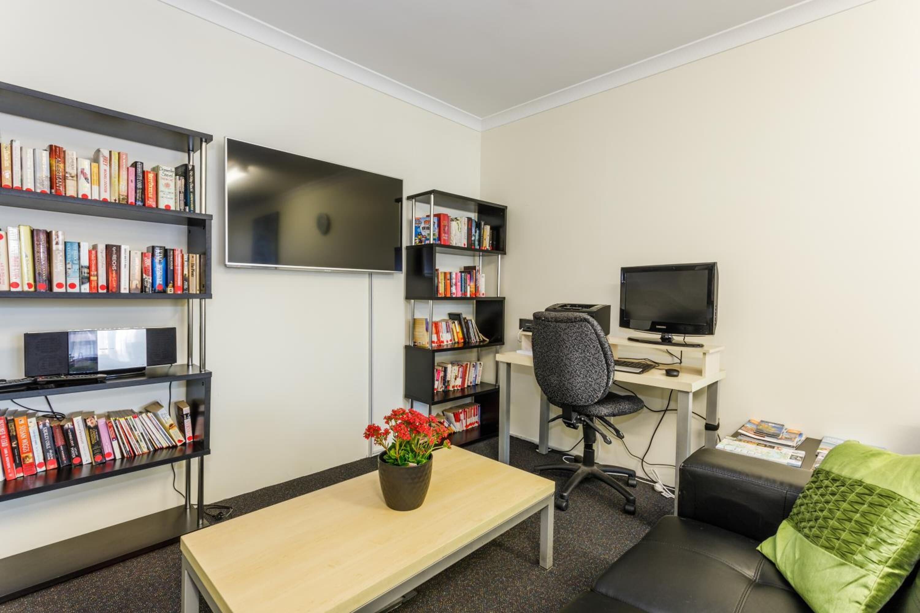 Un espacio de oficina moderno con dos estanterías, un escritorio con computadora, una silla y un televisor.