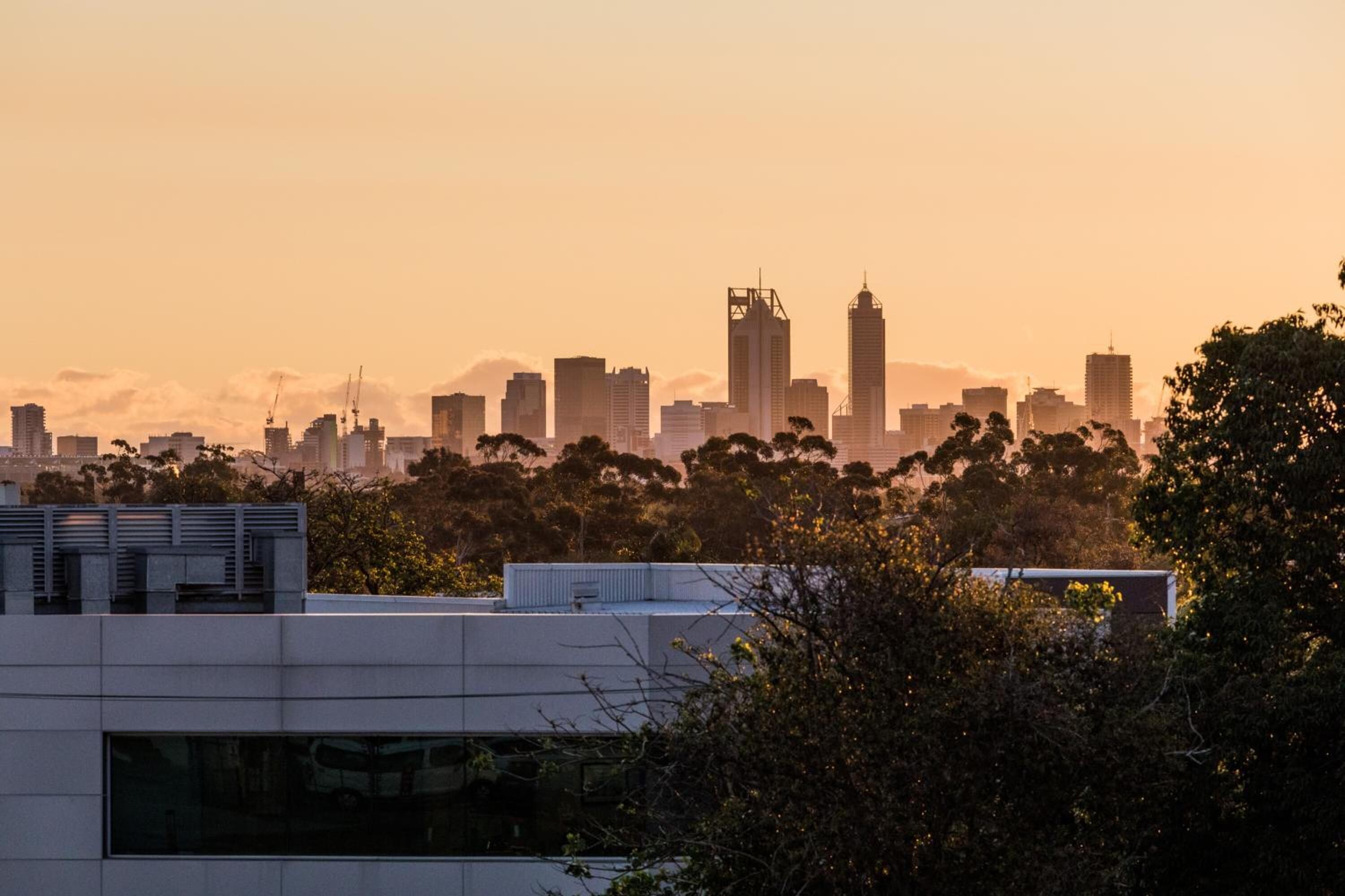 Un horizonte urbano al atardecer con edificios modernos y grúas de construcción.