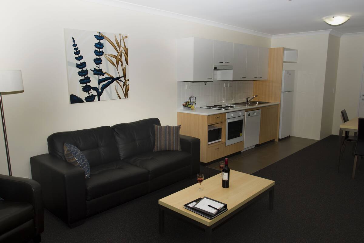A modern living room with a black sofa, a wooden coffee table, and a painting on the wall.
