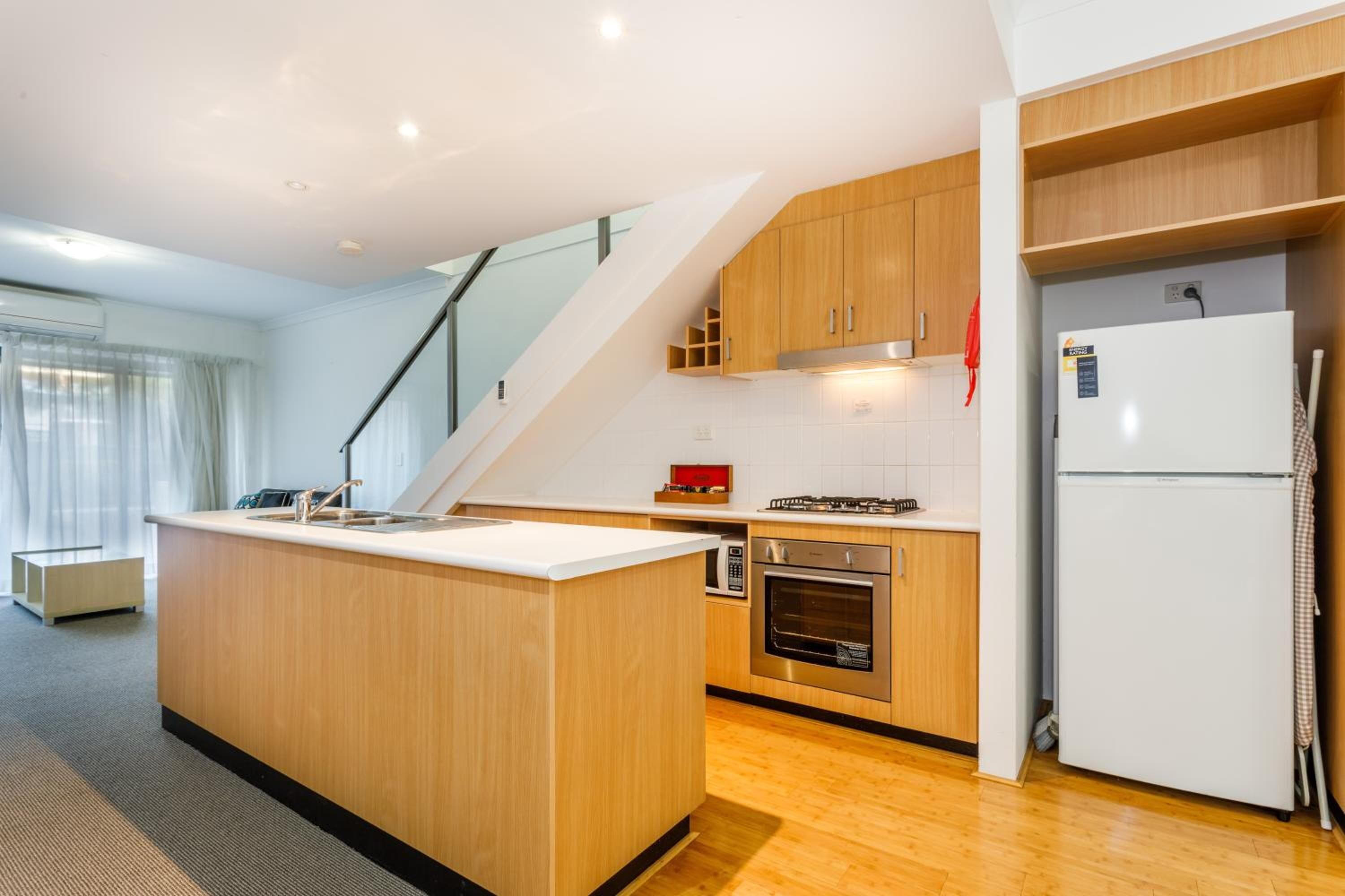 A modern kitchen with wooden cabinets, a built-in oven, a white refrigerator, and a small island with a sink.