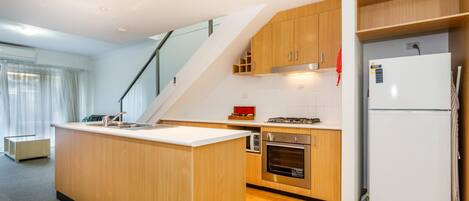 A modern kitchen with wooden cabinets, a built-in oven, a white refrigerator, and a small island with a sink.