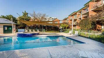 Una piscina al aire libre, sombrillas, sillones reclinables de piscina