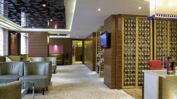 Eine moderne Hotelhalle mit gemustertem Teppich, einer Sitzecke mit Sofas, einem Fernseher auf einem Holzständer und einer Wand mit geometrischem Dekor.