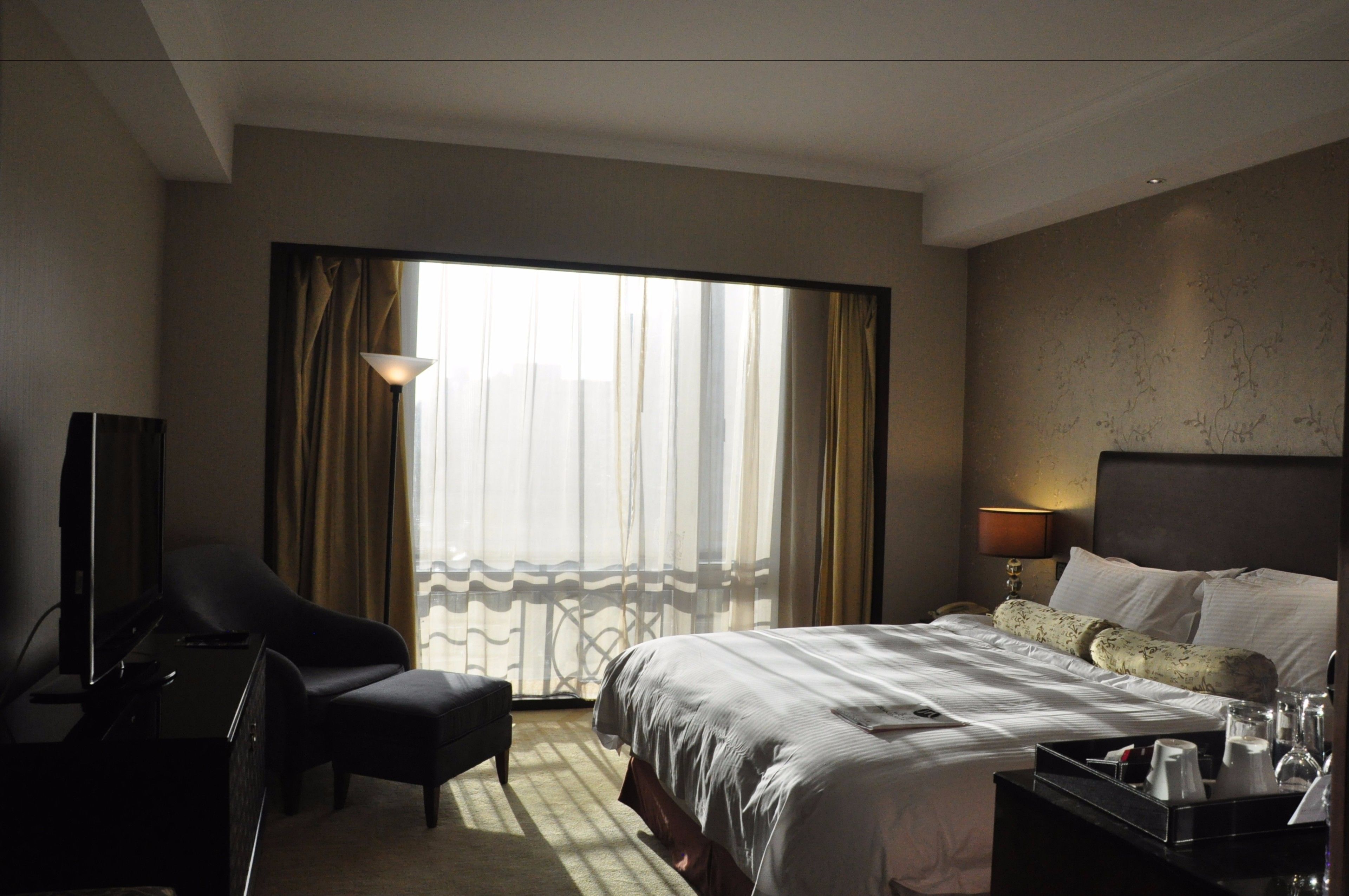 A hotel room with a large bed, a desk with a chair, a TV, and a window with curtains.